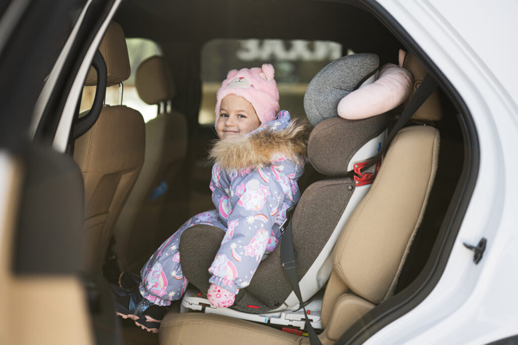 Child safety seat chair with baby girl is on back seat of car.